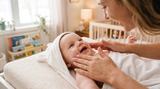 Smiling baby getting moisturiser applied to cheeks after bath